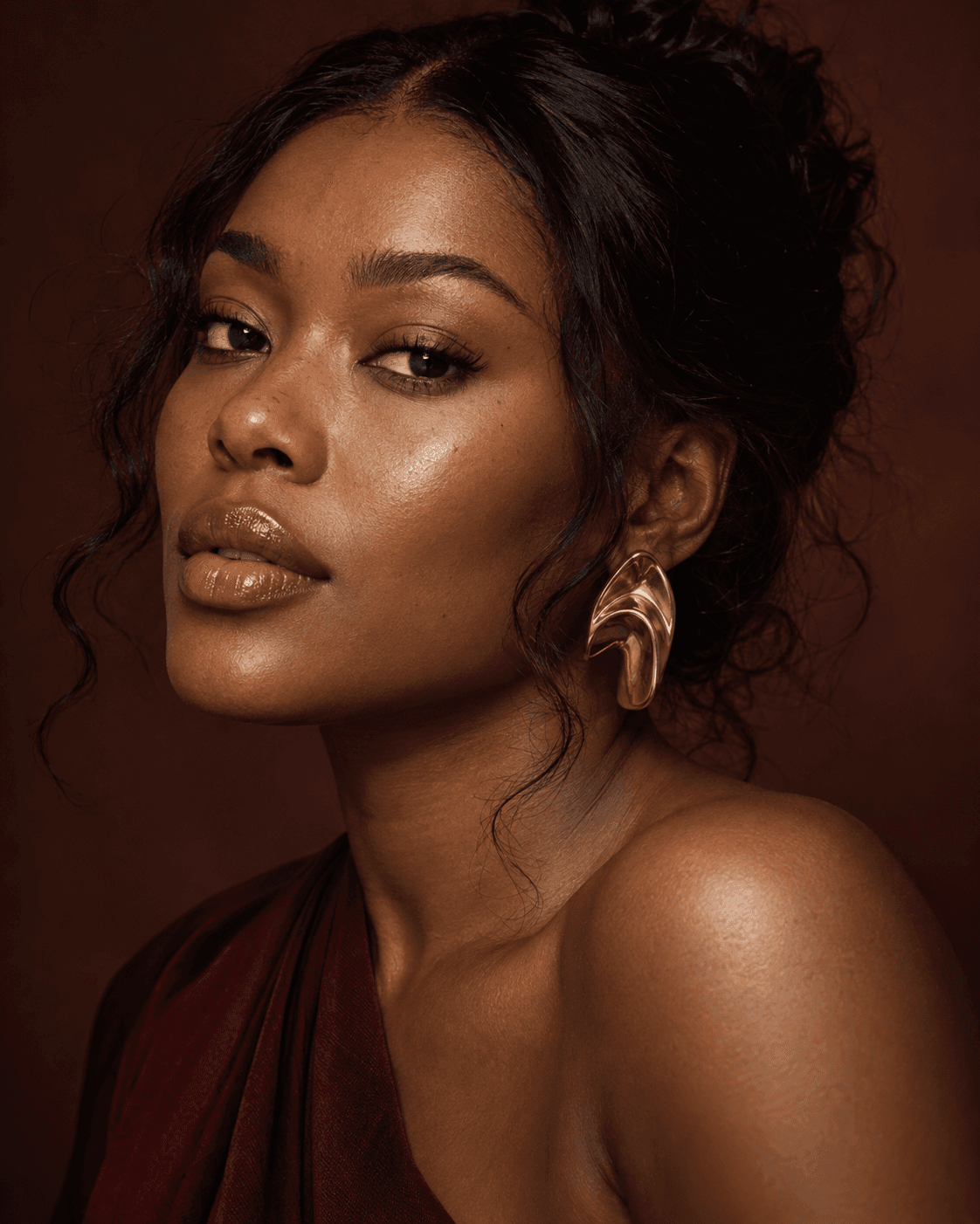 Editorial close-up showing luminous natural makeup and sculptural gold jewelry