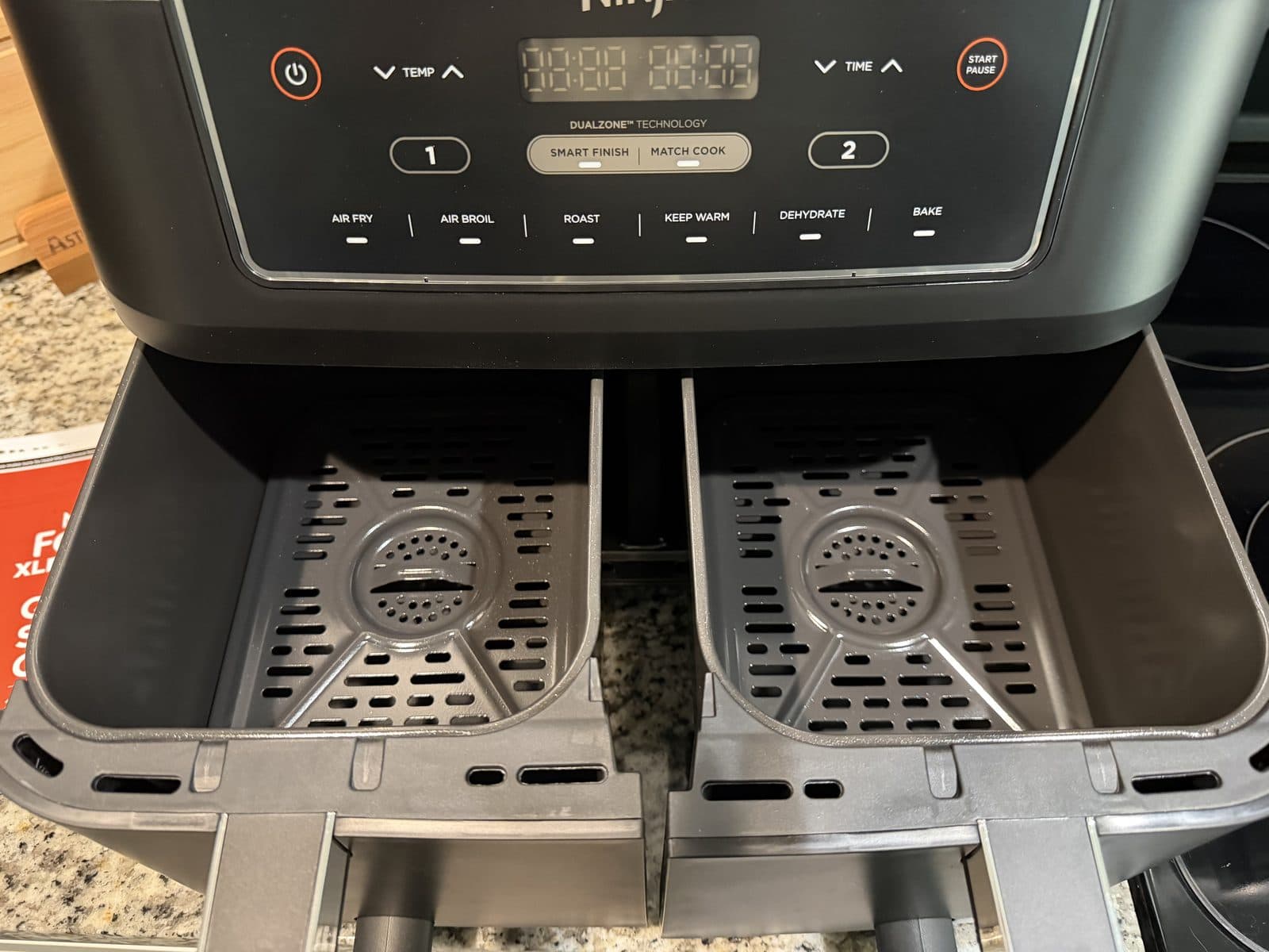 Both baskets of the Ninja Foodi XL DualZone air fryer pulled open to show two empty crisper plates, under a control panel with zone 1 and zone 2 buttons and Smart Finish and Match Cook settings.