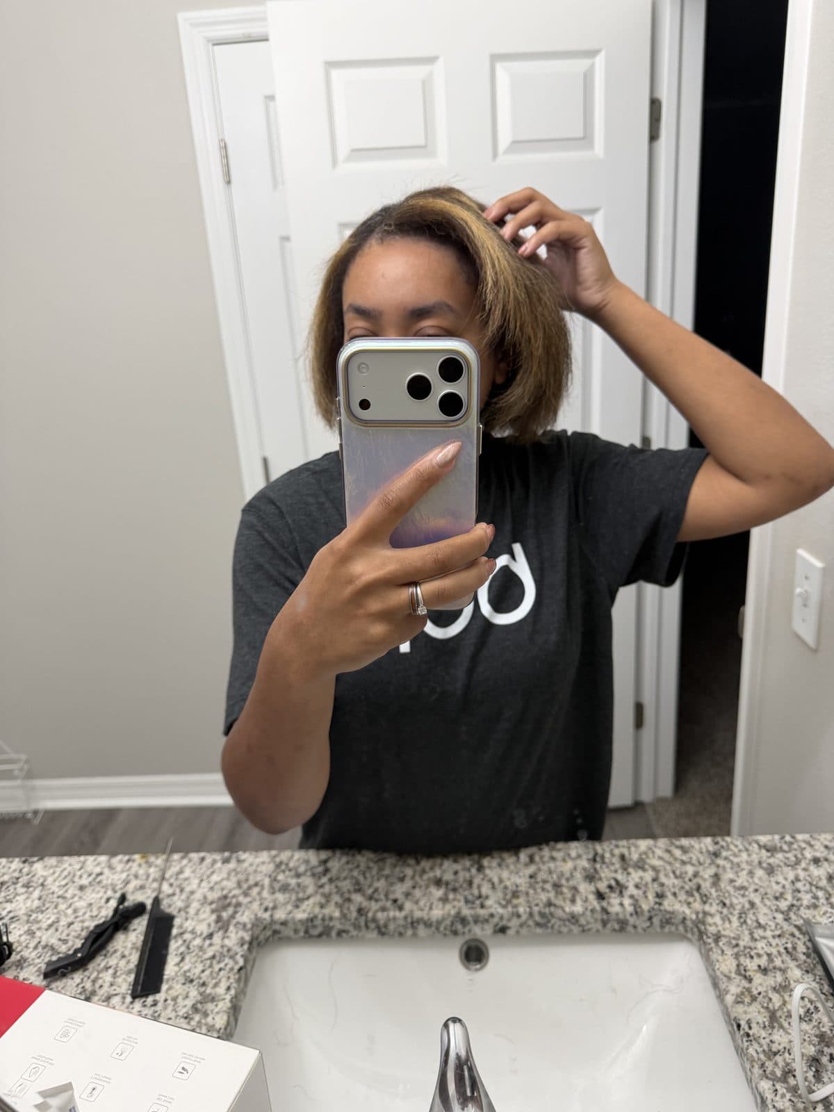 Mirror selfie of Martika after styling, her chin-length bob with honey highlights smooth and lifted at the crown as she runs a hand through the top.